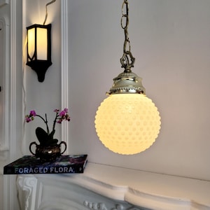 May include: A white milk glass pendant light with a chain and a brass fixture. The light is hanging from a white ceiling and is illuminating a white fireplace mantel.