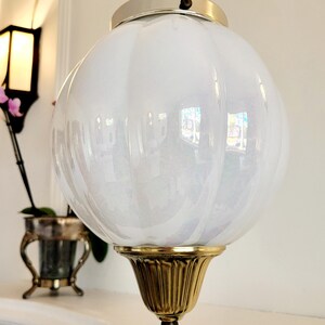 May include: A white, iridescent glass globe pendant light fixture with a gold metal base and a silver metal top.
