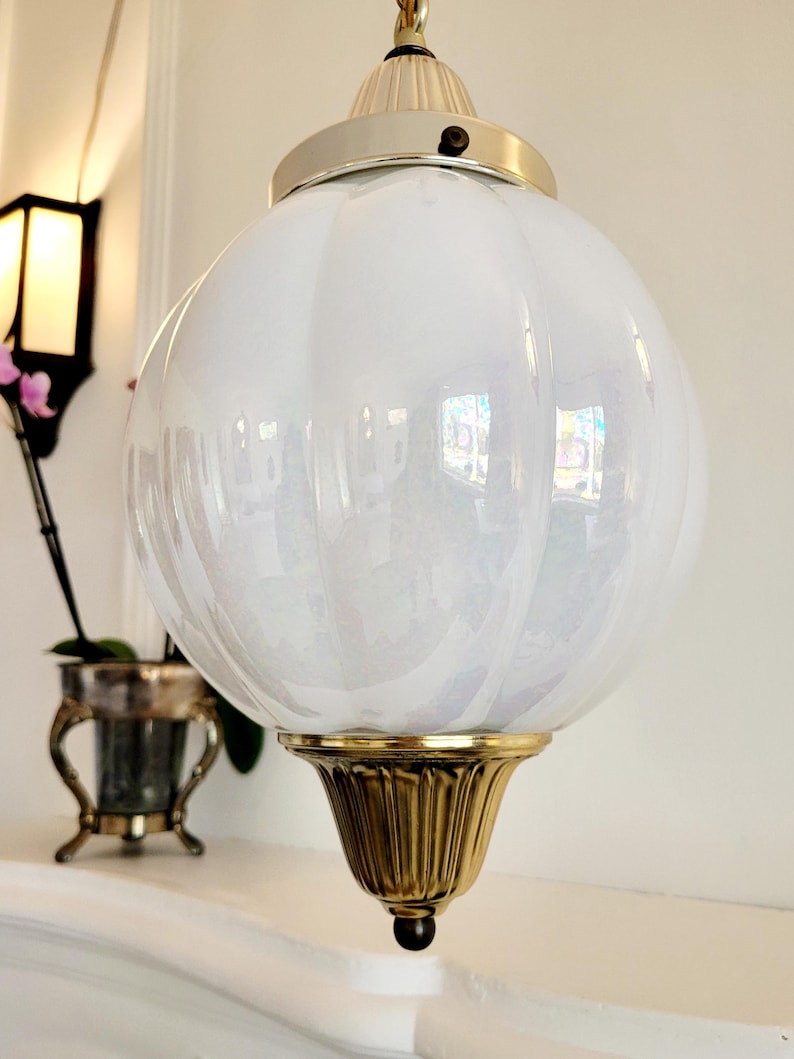 May include: A white, iridescent glass globe pendant light fixture with a gold metal base and a silver metal top.