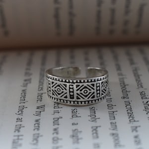 Puede incluir: Un anillo de dedo del pie de plata con un diseño geométrico. El anillo está hecho de metal y tiene un aspecto simple y elegante.