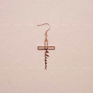 May include: Gold cross earring with the word "Faith" written in cursive on the bottom of the cross.