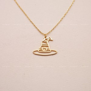Puede incluir: Un collar de oro con un colgante de sombrero de bruja. El sombrero está contorneado en oro y tiene un diseño a rayas.
