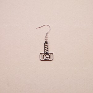 Può includere: Orecchino d'argento con un contorno nero di un martello, un simbolo popolare nella mitologia norrena.