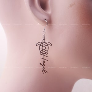 May include: Silver dangle earrings with a turtle silhouette and the word "Hazel" written vertically below it.