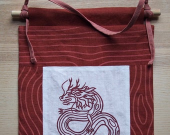 May include: A red fabric wall hanging with a white panel featuring a black and white line drawing of a dragon. The fabric has a wood grain pattern.