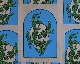 May include: A white skull with green leaves covering the eyes and mouth. The skull is on a blue background with a white border. The text "Sometimes I Alternate Days" is printed below the skull.