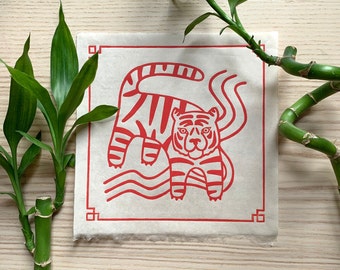 May include: Red and white illustration of a tiger on a cream-colored paper background. The tiger is depicted in a stylized, graphic design style. The tiger is surrounded by red wavy lines.