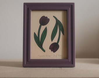 May include: A framed artwork featuring two black tulip illustrations with green stems and leaves. The artwork is set in a rectangular, purple frame. The text "Black tulips" is visible at the bottom of the artwork.