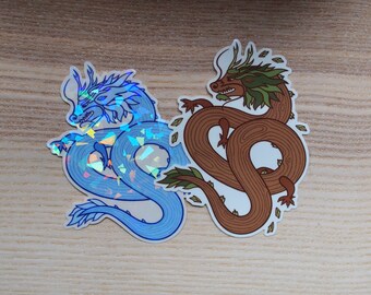 May include: Two dragon stickers, one blue with iridescent glitter and one brown with green leaves. The blue dragon is curled up with its head facing left, while the brown dragon is curled up with its head facing right.