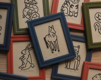 May include: A collection of framed illustrations of the Chinese zodiac animals. The frames are in various colors, including red, blue, and green. The illustrations are in black and white and depict a monkey, a snake, a tiger, a horse, a rabbit, and a dog.