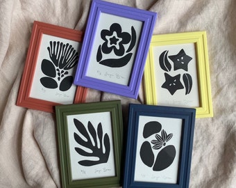 May include: Five framed prints with black and white abstract designs. The frames are in various colors, including purple, yellow, red, green, and blue. The prints feature different shapes and patterns, including flowers, stars, and leaves. The text on the prints reads "#12 Sugar Boo", "#14 Sugar Boo", "#15 Sugar Boo", "#17 Sugar Boo", and "#18 Sugar Boo".