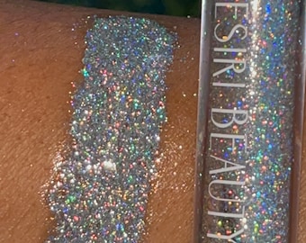 May include: A clear tube of iridescent glitter with the text "DESIRI BEAUTY" printed on the side. The glitter is shown applied to skin, creating a shimmering effect.