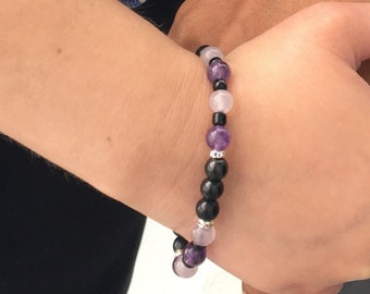 May include: A bracelet with black, purple, and pink beads. The bracelet is on a person's wrist.