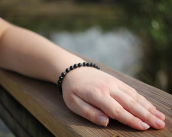 May include: A black beaded bracelet on a person's wrist. The bracelet is made of small, round beads.