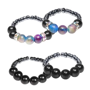 May include: Two beaded bracelets. One bracelet features black, iridescent, and blue beads with rhinestone accents. The other bracelet has black beads and silver-colored beads. The bracelets are on a white background.
