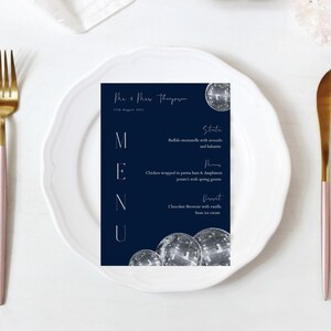 May include: A navy blue wedding menu card with white text. The menu includes a starter, main course, and dessert. The card is decorated with a silver disco ball graphic.