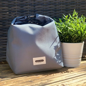 May include: A gray canvas lunch bag with a black and white label that reads "black+blum LONDON".