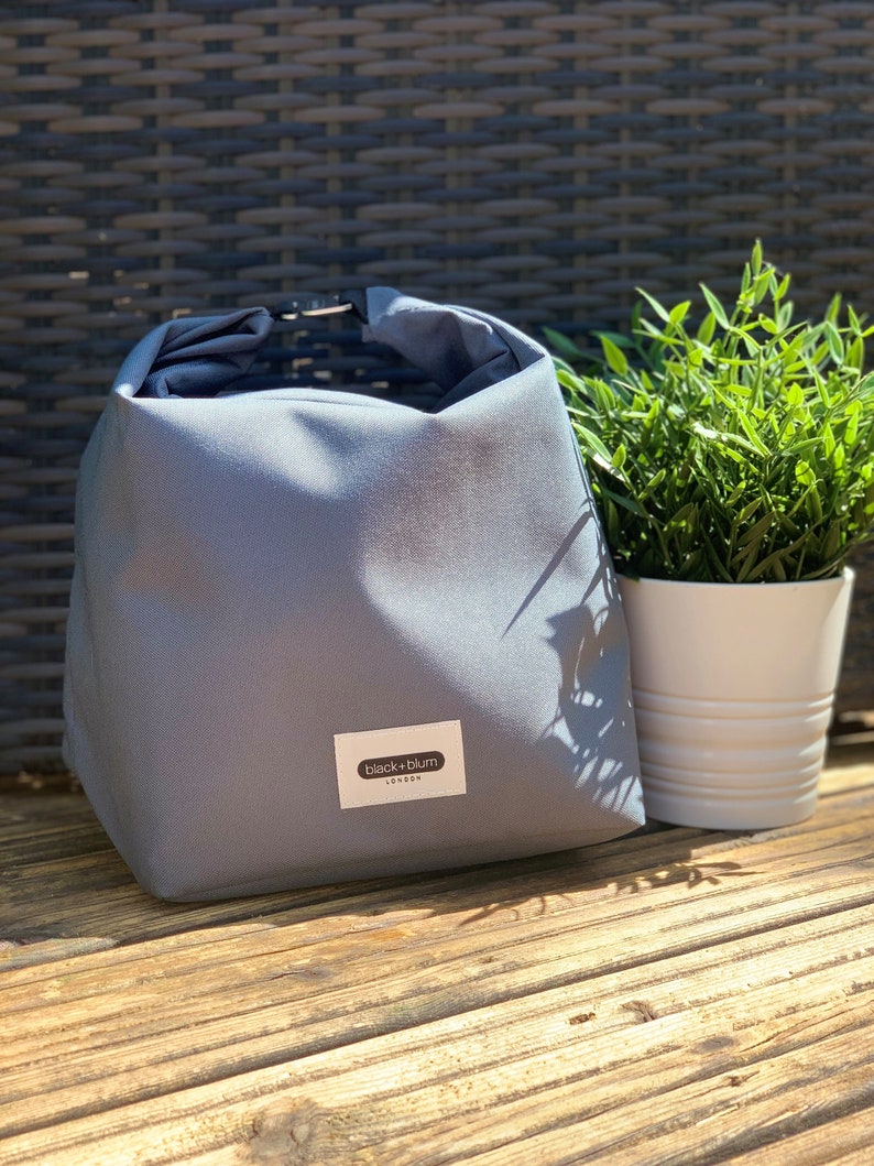 May include: A gray canvas lunch bag with a black and white label that reads "black+blum LONDON".