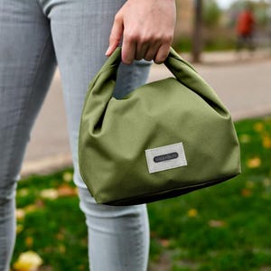 May include: A green canvas lunch bag with a white label that says "Lunchtime" on it.