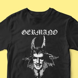 Op de afbeelding: Zwart t-shirt met een witte afbeelding van een man met geitenhoorns en het woord "GERMANO" boven de afbeelding in een gotisch lettertype. De afbeelding is een zwart-wit illustratie.