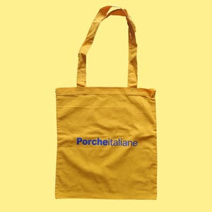 Può includere: Una borsa di tela gialla con testo blu che dice "Porcheitaliane".