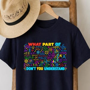 May include: A navy blue short-sleeved t-shirt featuring a colourful graphic print of various mathematical and scientific symbols and formulas. The text on the shirt reads, "WHAT PART OF" at the top and "DON'T YOU UNDERSTAND" at the bottom in bright colours.