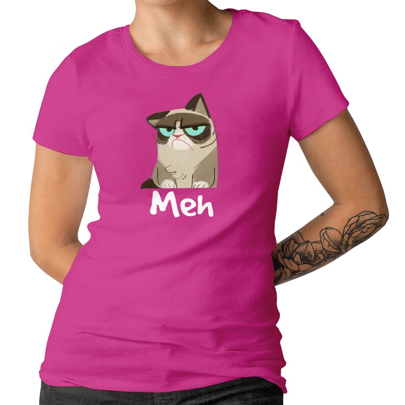 May include: A pink women's t-shirt featuring a cartoon image of a grumpy cat with the word "Meh" printed below the cat.