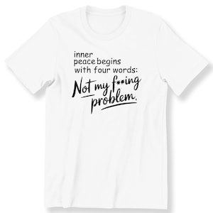 Op de afbeelding: Wit T-shirt met zwarte tekst die luidt: "inner peace begins with four words: Not my f***ing problem."