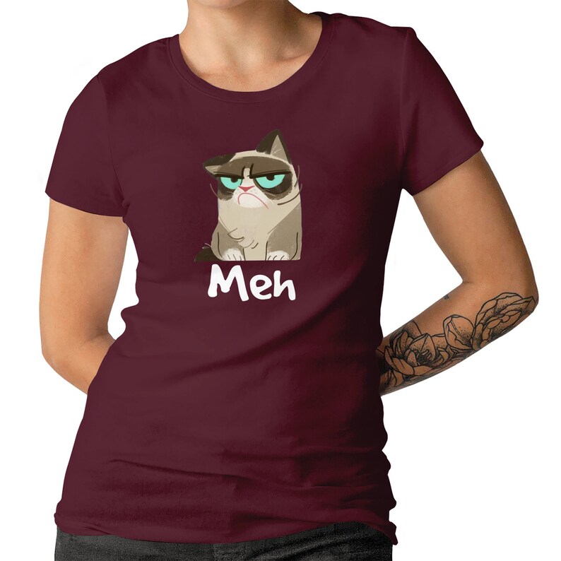 May include: A maroon t-shirt featuring a cartoon image of a grumpy cat and the word "Meh" printed on the front.