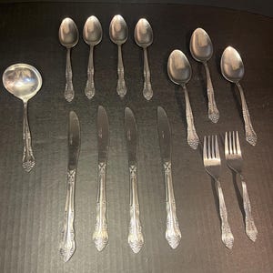 May include: A set of silverware with a decorative design. The set includes spoons, forks, and knives. The silverware is made of stainless steel and has a polished finish.