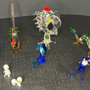 May include: A collection of eight glass animal figurines, including a white cat, a blue fish, a green dragon, a red rooster, and a clear elephant. The figurines are all hand-blown and have intricate details.