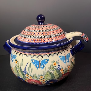 May include: A blue and white ceramic soup tureen with a floral and butterfly design. The tureen has a lid and a matching ladle.