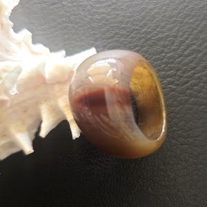 May include: A brown and white agate ring with a gold band. The ring is carved with a design of a bird.