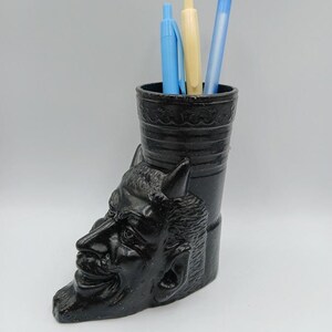 May include: Black ceramic desk organizer shaped like a devil's head with three pens inside.