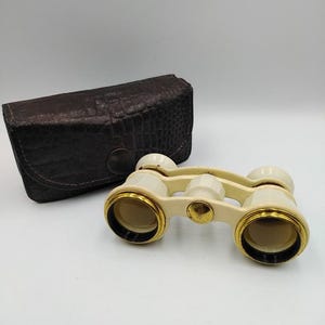 Op de afbeelding: Witte operaglazen met gouden accenten en een bruin leren etui.