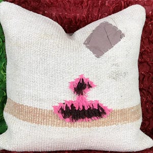 May include: White throw pillow with a pink and brown geometric design. The pillow has a beige stripe and a gray patch sewn on.