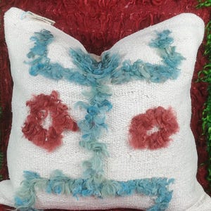 May include: White throw pillow with a blue and red design. The design features two large circles in red and a blue pattern in the center.