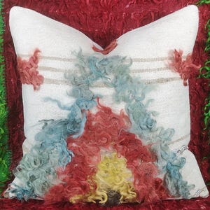 May include: White throw pillow with a colorful, abstract design. The design features red, blue, yellow, and brown curly fibers.