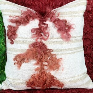 May include: White pillow with a striped pattern and a large, fluffy, pink and red accent. The accent is made of curly fibers and is shaped like a tree.