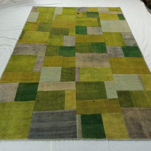 Puede incluir: Una alfombra de patchwork con una variedad de cuadrados verdes, marrones y beige. La alfombra está hecha de diferentes telas y tiene un borde cosido a mano.