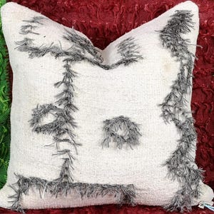 May include: White throw pillow with a gray fringe design. The pillow has a textured surface and is made of a soft, fluffy material.