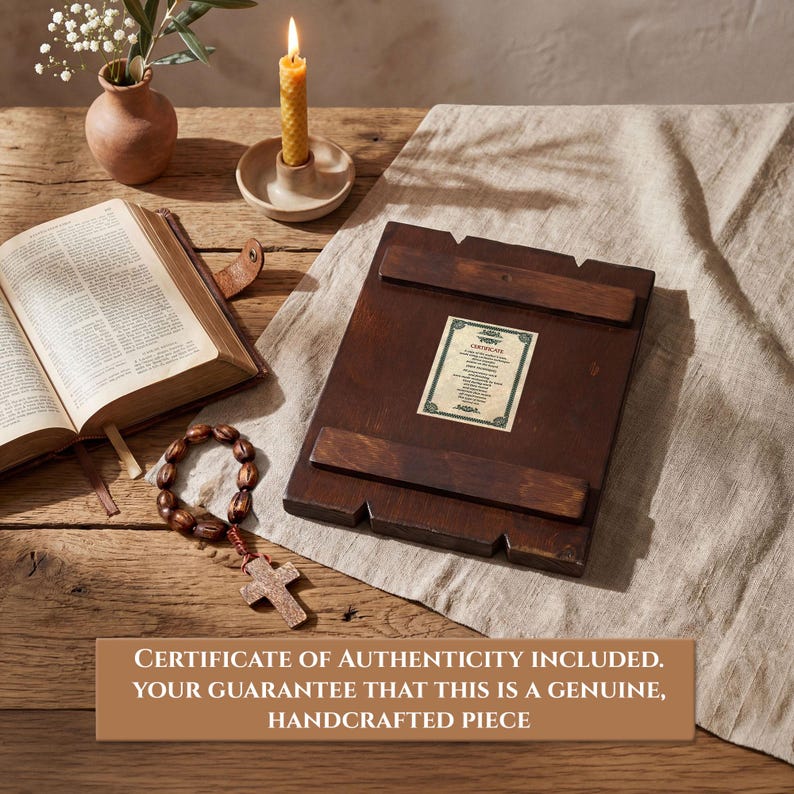 Pode incluir: &Iacute;cone religioso de madeira escura com certificado de autenticidade, sobre tecido bege. Um ros&aacute;rio com cruz, um livro aberto, uma vela acesa e um pequeno vaso com flores tamb&eacute;m s&atilde;o vis&iacute;veis. O texto diz: CERTIFICADO DE AUTENTICIDADE INCLU&Iacute;DO.
