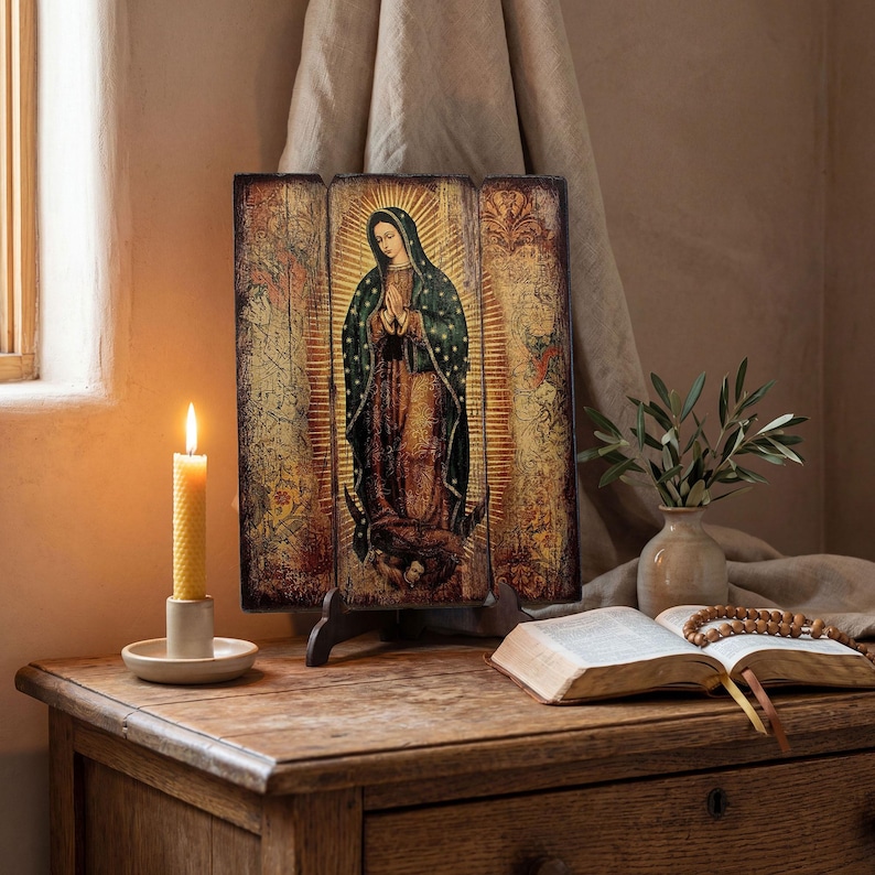 Pode incluir: Um &iacute;cone religioso de madeira retratando uma figura em um manto escuro com uma aur&eacute;ola, exibido em um suporte de madeira. Uma vela acesa em um suporte branco, um livro aberto e um vaso com vegeta&ccedil;&atilde;o est&atilde;o em uma mesa de madeira.