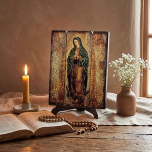 Pode incluir: Um &iacute;cone religioso de madeira retratando uma figura em um manto verde com uma aur&eacute;ola dourada. O &iacute;cone &eacute; exibido em um suporte de madeira. Uma vela acesa, um livro aberto, um ros&aacute;rio e um vaso de flores brancas tamb&eacute;m est&atilde;o presentes.