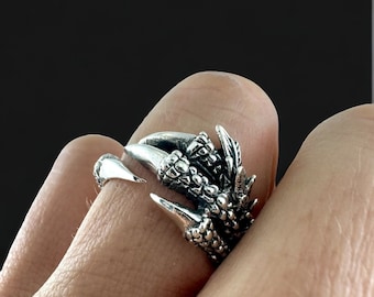 Puede incluir: Un anillo de plata con forma de garra de dragón con escamas texturizadas detalladas.