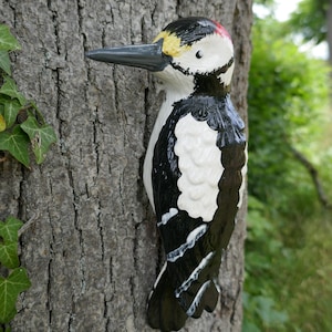 Peut inclure: Une figurine en bois de pic noir et blanc avec une cr&ecirc;te rouge, perch&eacute;e sur un tronc d'arbre. La figurine est peinte avec des d&eacute;tails r&eacute;alistes, y compris des plumes noires et blanches et un bec jaune.