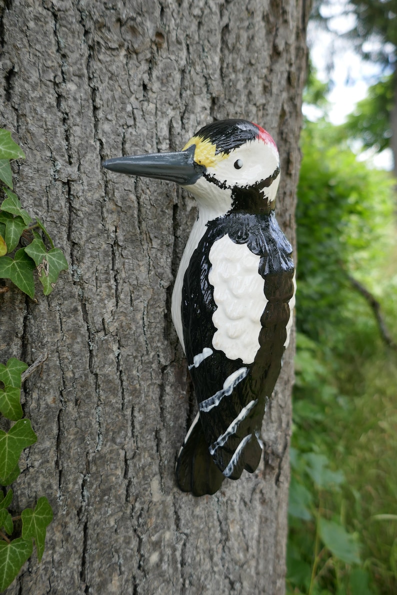 Peut inclure: Une figurine en bois de pic noir et blanc avec une cr&ecirc;te rouge, perch&eacute;e sur un tronc d'arbre. La figurine est peinte avec des d&eacute;tails r&eacute;alistes, y compris des plumes noires et blanches et un bec jaune.
