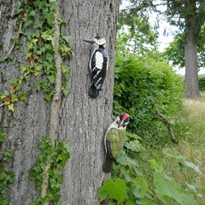 Peut inclure: Deux figurines d'oiseaux en bois fix&eacute;es &agrave; un tronc d'arbre. L'oiseau de gauche est noir et blanc avec un bec rouge. L'oiseau de droite est vert avec une t&ecirc;te rouge et des yeux noirs.