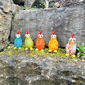 Könnte beinhalten: Fünf bunte Mosaik-Keramikhühner mit roten Kämmen und gelben Füßen. Die Hühner sind in einer Reihe auf einem grauen Stein mit grünem Moos angeordnet.