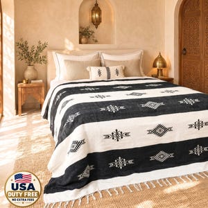 Peut inclure: Un jeté de lit noir et blanc orné de rayures horizontales et de motifs géométriques, terminé par une bordure à franges. Le jeté est disposé sur un lit avec des oreillers blancs et beiges, présentant un design contrasté aux motifs complexes.